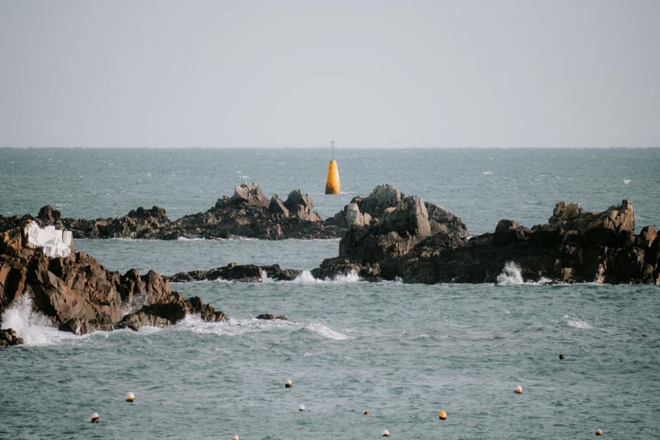 A granite reef and beacon off Bordeaux Harbour on a grey-green sea