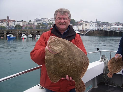 An angler holds up a large turbot in St Peter Port Harbour
