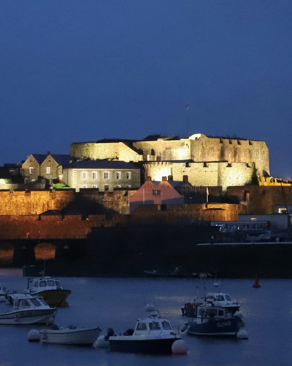 Castle Cornet lit up at dusk behind moored boats