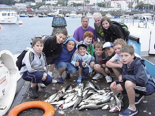 Children crouch round a pile of mackerel on deck, St Peter Port behind
