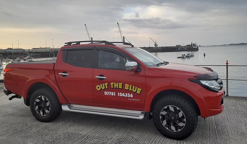A red pickup sign-written with Out the Blue and the phone number, on the quay